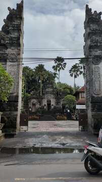 Bali Street Traffic in Front of Pura Dalem Ubud Temple, Motorbikes Passing Traditional Stone Gates and Palm Trees