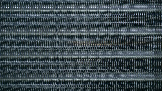 Close up metal fins, tubes of heat exchanger or radiator grille from an air conditioning unit, revealing intricate patterns and texture of cooling system. Air conditioner condenser coil moving upwards