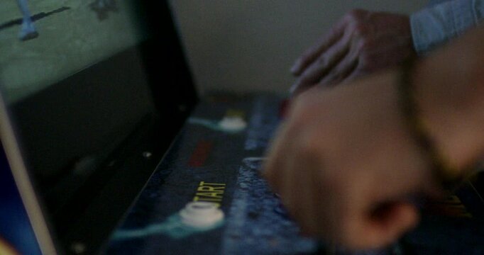 Close up of two people playing a classic arcade machine with joysticks and buttons