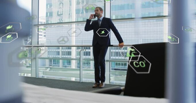 Walking man wearing dark suit talking on phone, office atrium with glass railing and green icons