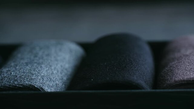 Macro shot showing variety of colorful comfortable folded socks arranged neatly in dark container, with slow camera movement revealing soft texture of warm winter clothing. Man socks inside box