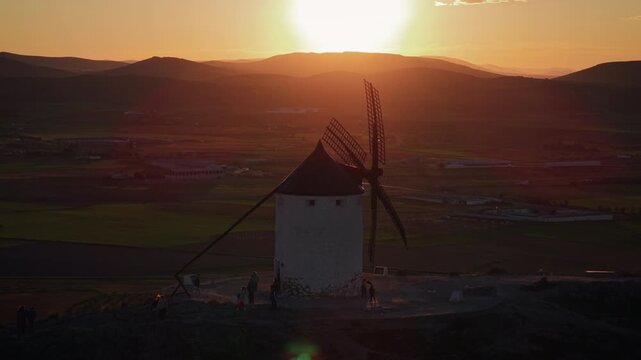Iconic windmills of Consuegra in Castilla La Mancha, Spain, during a stunning golden hour sunset, with tourists admiring the breathtaking scenic landscape