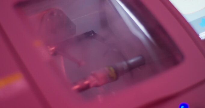 Close up of optical lens edger machine cutting an eyeglass lens in laboratory with water spray