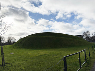 Naklejka premium Grassy earthwork mound and green hill in a park with dramatic cloudy sky in Edinburgh, Scotland, UK historic landscape scene