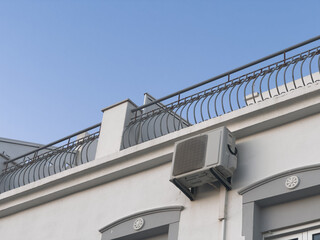 Naklejka premium Modern residential building exterior with light cream siding, multiple air conditioning units, reflective blue windows, and small balcony with metal railing, set against clear blue sky on bright sunny