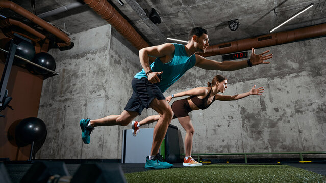 Man and woman performing functional training movement with forward reach in gym. Concept of mobility training, balance development, fitness program and athletic performance