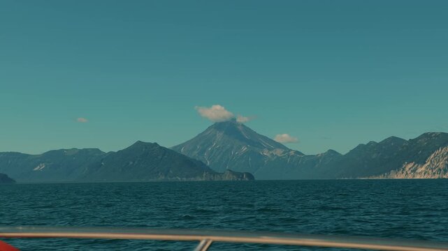 Stunningly beautiful view from yacht of mountain ranges on coast and majestic volcano with peak in clouds. Concept of freedom and pacification