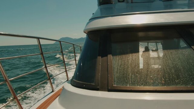 Yacht moves at high speed through sea bay leaving seething wake on water and silhouette of couple in cabin through glass. Travel and tourism concept