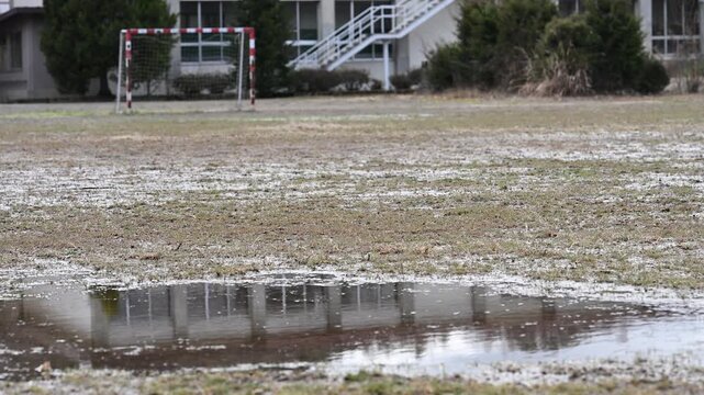 閉校となった小学校の荒れた校庭。雨上がりのグランドの水たまりと残されたサッカーゴール。冬の風景。