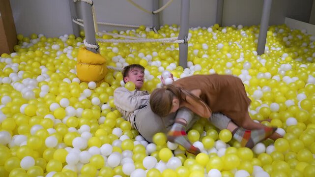 Active leisure: young boy and girl engage in playful scuffle within large, yellow-white ball pit at amusement area.