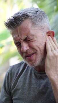 Man suffering ear pain and holding ear outdoors