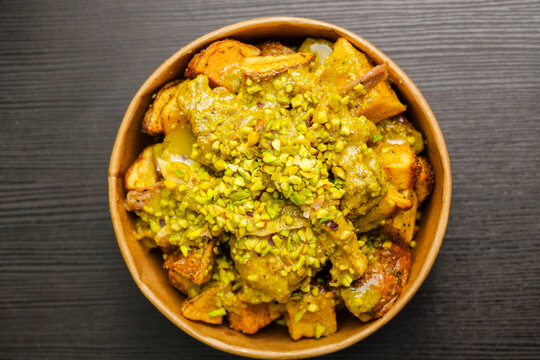 Porzione di patate al forno con salsa di pistacchio e granella di pistacchio servite in un contenitore di cartone da asporto