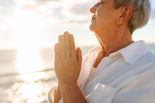 A gray-haired woman enjoys the seascape at sunset. A relaxed elderly woman strolls along a sandy beach, feeling free. Concepts for relaxation and retirement.