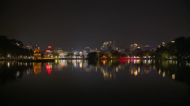 Scenic nighttime illumination of Hanoi's skyline reflecting on Hoan Kiem Lake, featuring iconic ancient Turtle Tower and Ngoc Son Temple with Huc Bridge