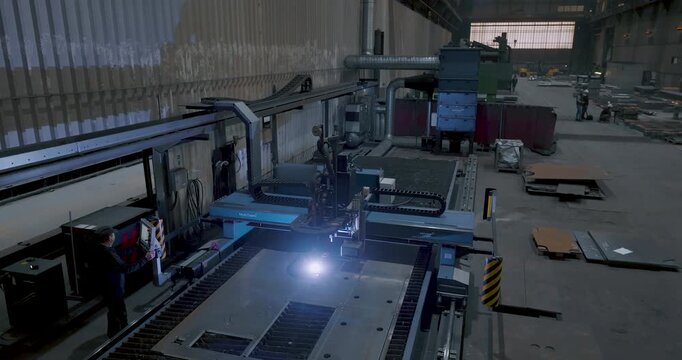 CNC machine operator controlling an automatic laser cutting machine in a large metal factory