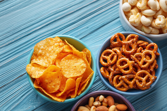 Colorful snack assortment with chips pretzels nuts and dip on blue wooden background with copy space