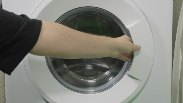 A hand opens the door of a washing machine in a home environment.