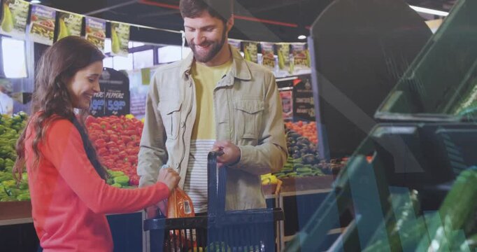 Woman picking bagged carrots and placing into black basket, man steadying, both shopping groceries