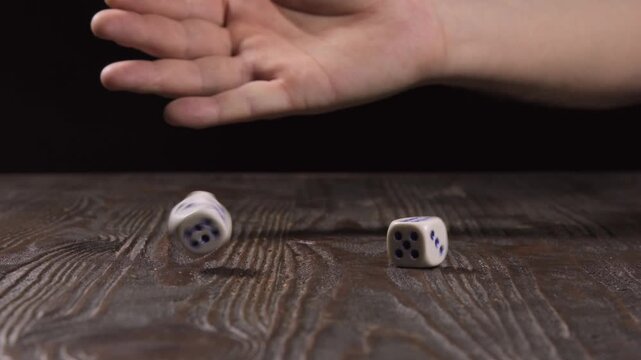 Close-up of a hand shuffling dice and then throwing them on a wooden table against a black background