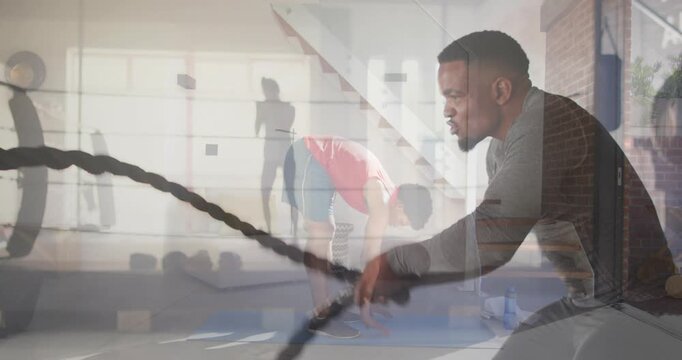 Man gripping and driving battle ropes in gym, creating ghosted rope waves during group training