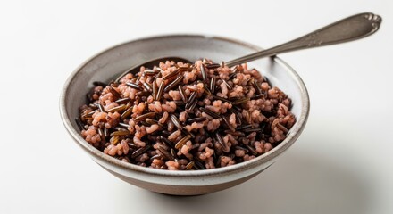 Fototapeta premium Cooked wild rice is served in a ceramic bowl with a metal spoon against a white background.