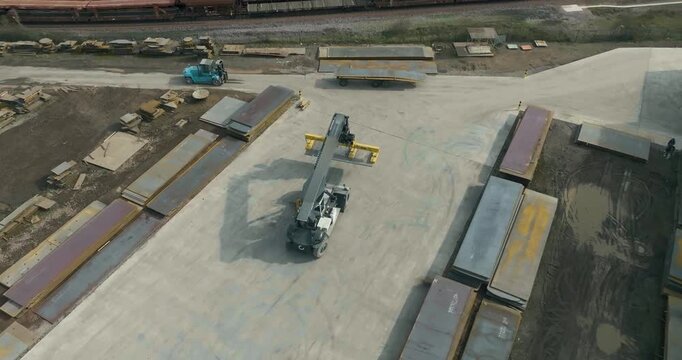 Wide aerial view of reach stacker and forklift working in a large industrial metal storage yard