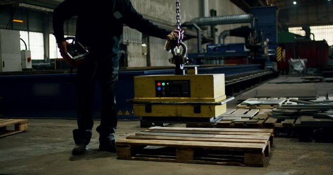 Factory worker using an industrial magnetic lifter to move metal parts in a workshop