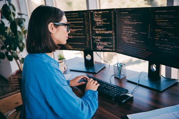 Female programmer coding at a multi monitor workstation in a modern office loft