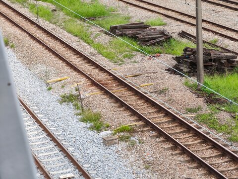 Multiple parallel railway tracks with steel rails, sleepers, gravel ballast, and patches of grass, viewed from elevated position in railway yard.  