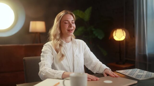 Young woman finishing her work with relief, stretching her body after using a laptop, relaxing and releasing tension at home in a calm indoor setting.