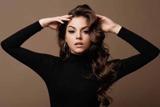 Elegant young woman with voluminous wavy hair and striking makeup posing confidently