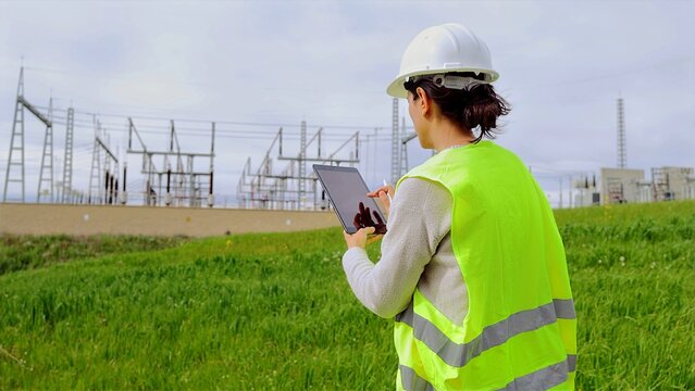 Female engineer observing a power station at a renewable energy facility, utilizing a tablet to manage grid operations and ensuring the sustainability of critical infrastructure