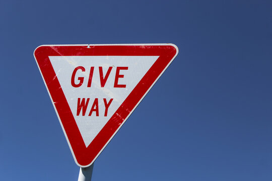 Closeup of a "GIVE WAY" road sign isolated against a blue sky commonly known in some regions as a yield sign.  Transportation design element. Abstract banner with copy space.
