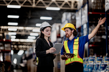 Fototapeta premium A professional Caucasian woman leading her team through a modern warehouse facility. She holds a tablet and stylus, pointing out details to male coworkers in a focused, collaborative environment.