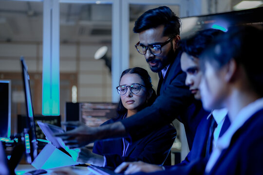 Senior software architect mentoring diverse development team on backend code. Agile scrum master leading sprint review in modern blue light tech office.