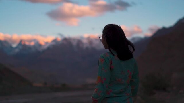 Silhouette shot of tourist woman walking against snowy Himalayas during sunset in Spiti Valley, India. Travel and holidays concept.  Girl enjoying natural fresh atmosphere in mountains.