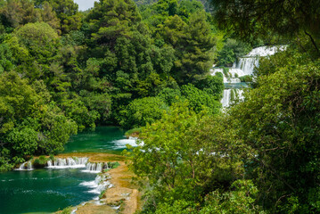 Fototapeta premium Stunning series of cascading waterfalls flowing through lush green forest with turquoise pools and mineral-rich terraces, creating vibrant, untouched natural paradise. Krka National Park is in Croatia