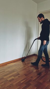 Man vacuuming wooden floor in empty room cleaning house slow motion vertical video