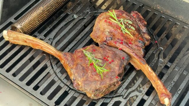 Grilling two large tomahawk steaks with herbs in a backyard setting on a warm day