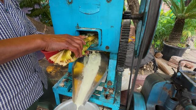Street vendor making fresh sugarcane juice with a crusher machine.
