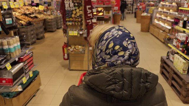 Lady wearing headscarf scrutinizes products on supermarket shelves carefully