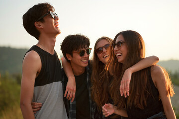 Fototapeta premium Four friends embracing and laughing together outdoors at sunset. Generative AI.