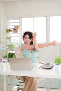 Asian young adult woman stretching arms taking active health break remote work home office improved focus posture wellbeing freelancer productivity digital nomad