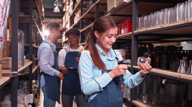 Professional female worker scanning products with barcode reader in warehouse. Team of diverse colleagues working in background. Concept of logistics and stock control.