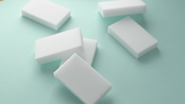 Melamine sponges fall from above onto mint surface in minimal household cleaning concept with soft light and simple top view