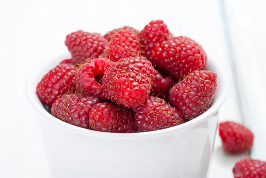 raspberry fruits at white ceramic cup, on bright wood table