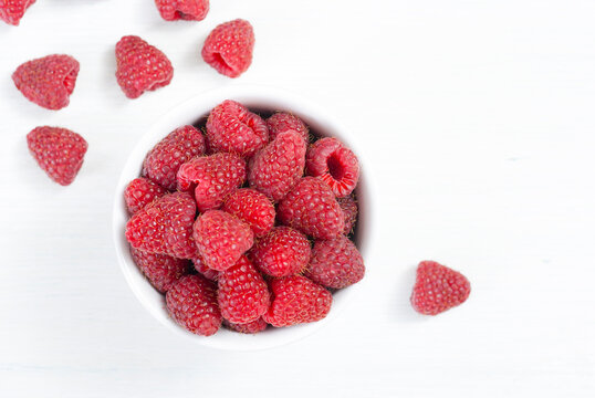 raspberry fruits at white ceramic cup, on bright wood table