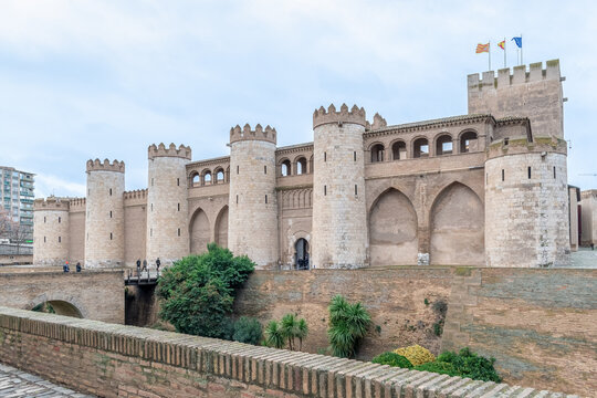 Aljaferia Palace, the seat of the Cortes of Aragon, with regional flags on medieval battlements. Historic Mudejar architecture and ramparts. Zaragoza, Spain - November 29, 2021