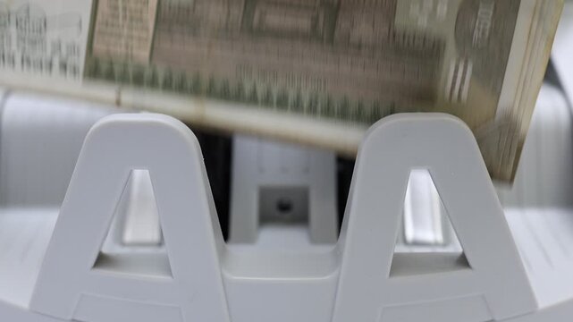 Macro shot of banknote counting machine with Indian rupee (INR) money. Automatic currency counter equipment processing 500 rupees with Red Fort vignette. Finance and banking industry in India.