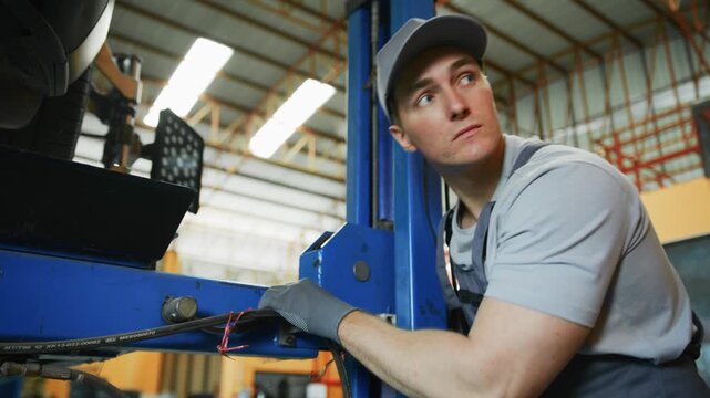Focused professional auto mechanic adjusting car lift for undercarriage inspection in garage
